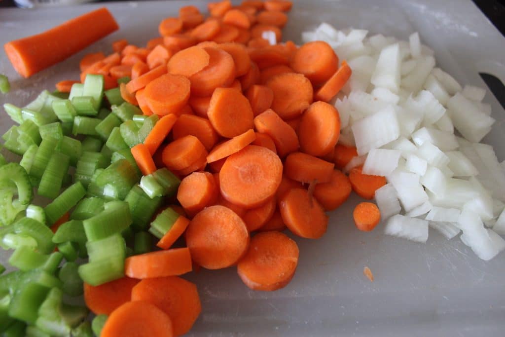Slices of celery, carrots, and diced onion on a plastic cutting board.
