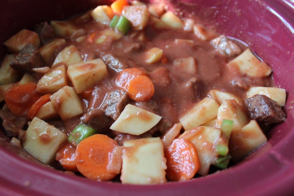 Beef stew with chunks of celery, carrot, and potato in a reddish bowl.