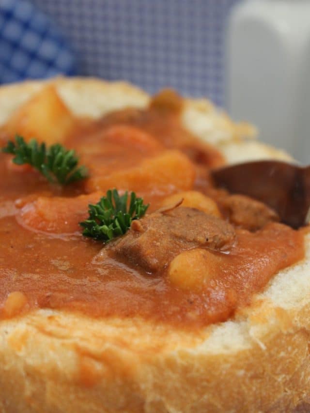 Very closeup view of beef stew in a bread bowl with springs of green herbs.