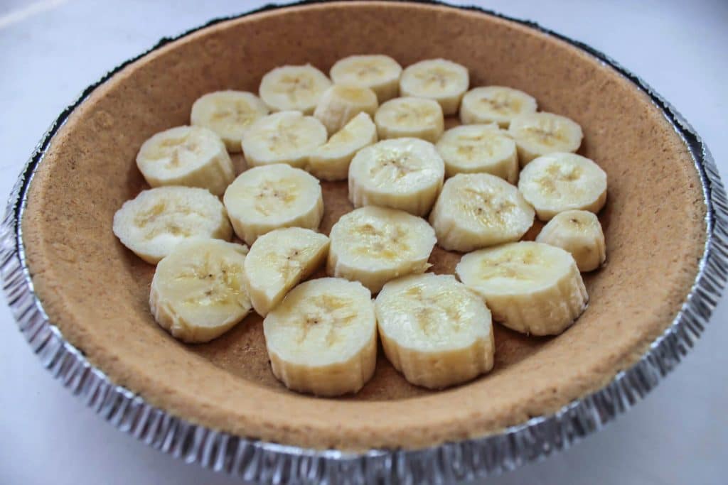 A graham cracker crust with slices of banana lining the bottom.