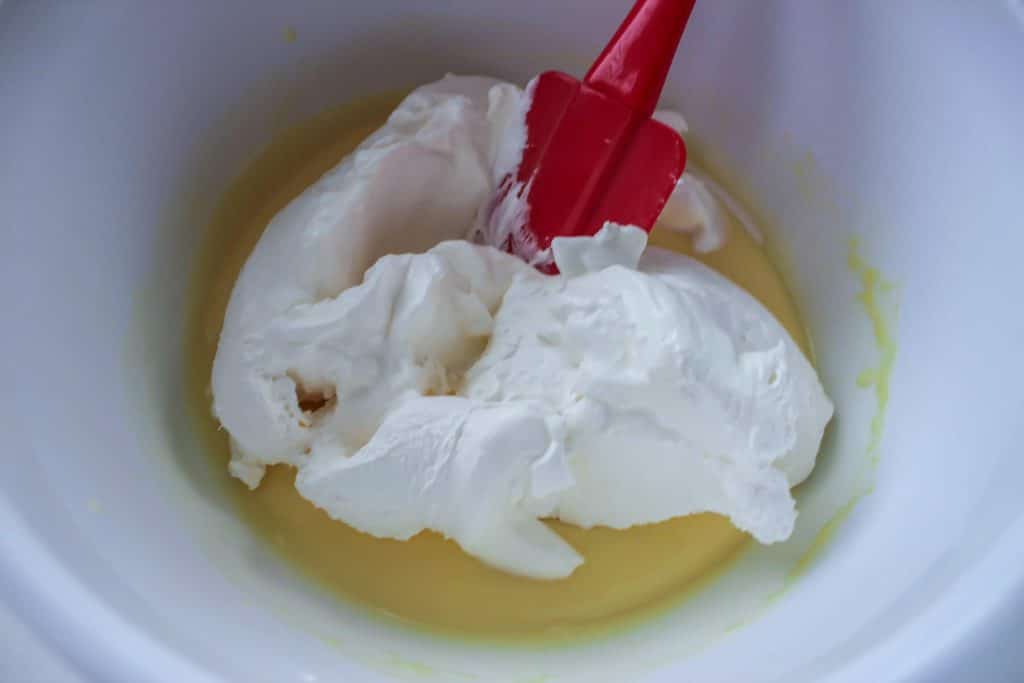 A red spatula folding cool whip into pudding.