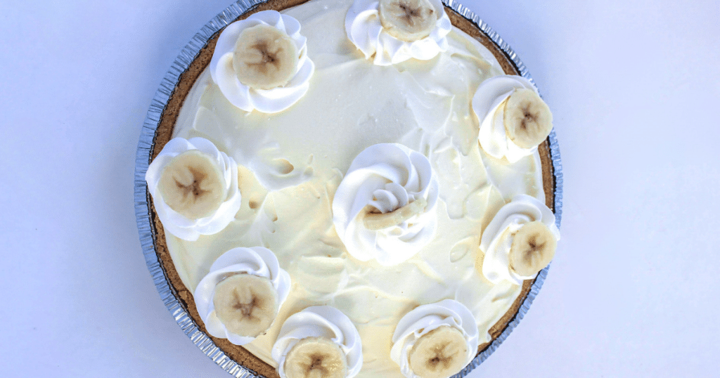 An overhead view of a whole banana cream pie topped with dollops of whipped cream and banana slices.