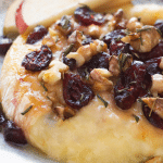 Closeup of gooey baked brie topped with cranberry sauce, honey, walnuts, and rosemary.