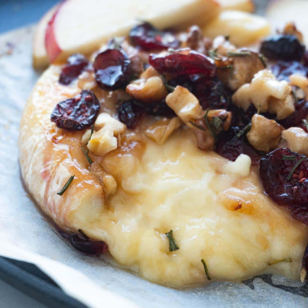 A closeup of baked brie topped with cranberries and walnuts.