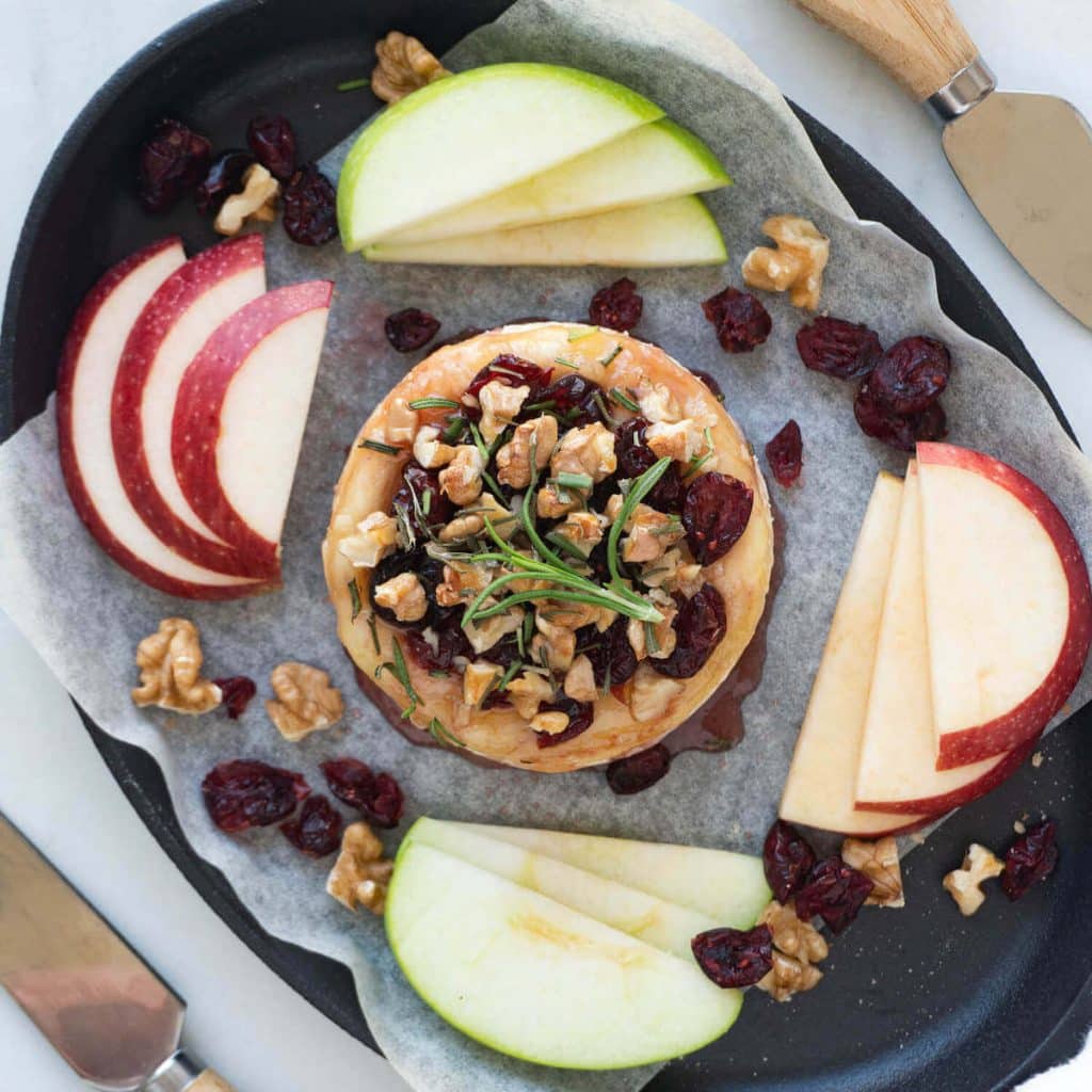 Cranberry baked brie surrounded by slices of green and red apples.
