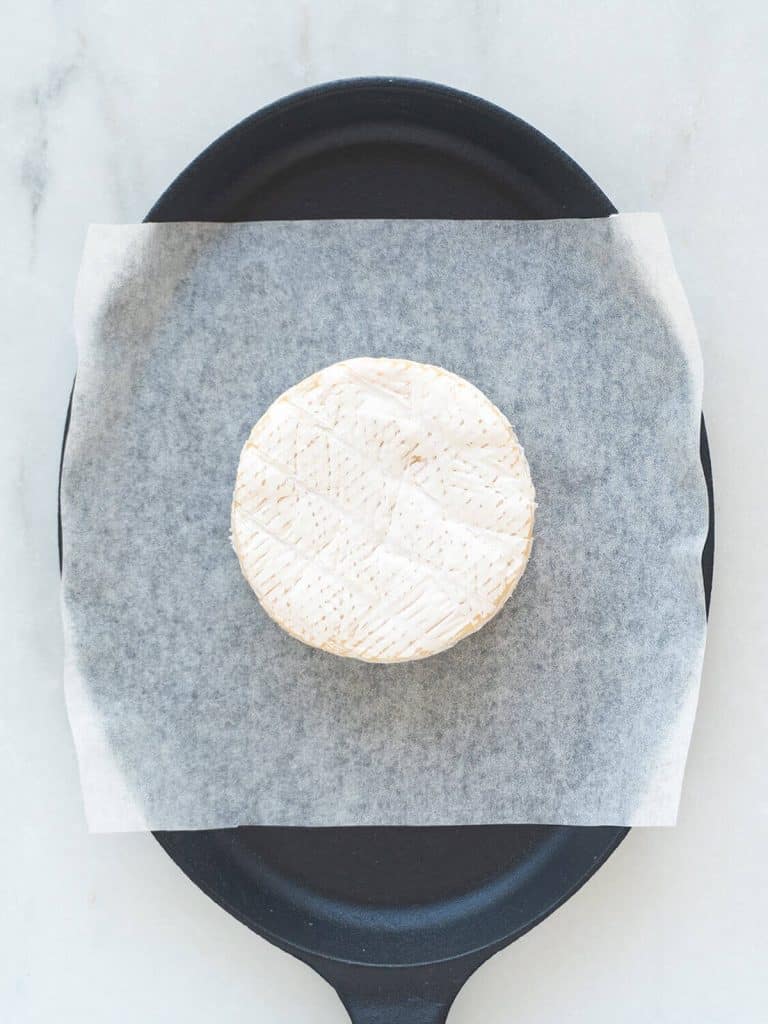 A wheel of brie is on a parchment paper sheet in a baking dish.