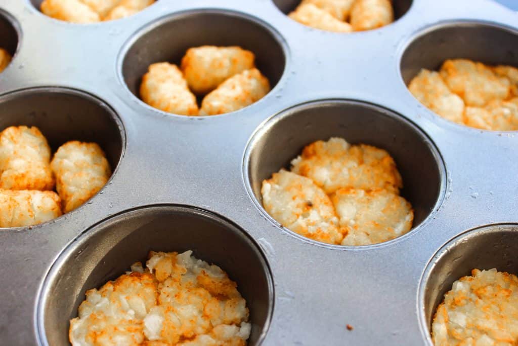 Tater tots in a muffin pan: half are smooshed down and the other half are whole tots still.