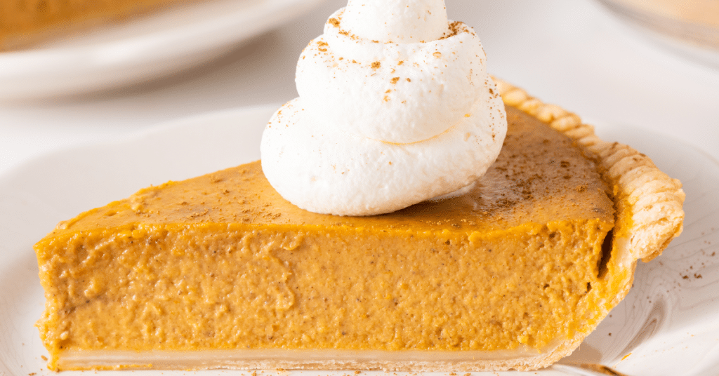 Maple pumpkin pie on a white plate, topped with whipped cream and sprinkled with a spice like cinnamon or nutmeg.