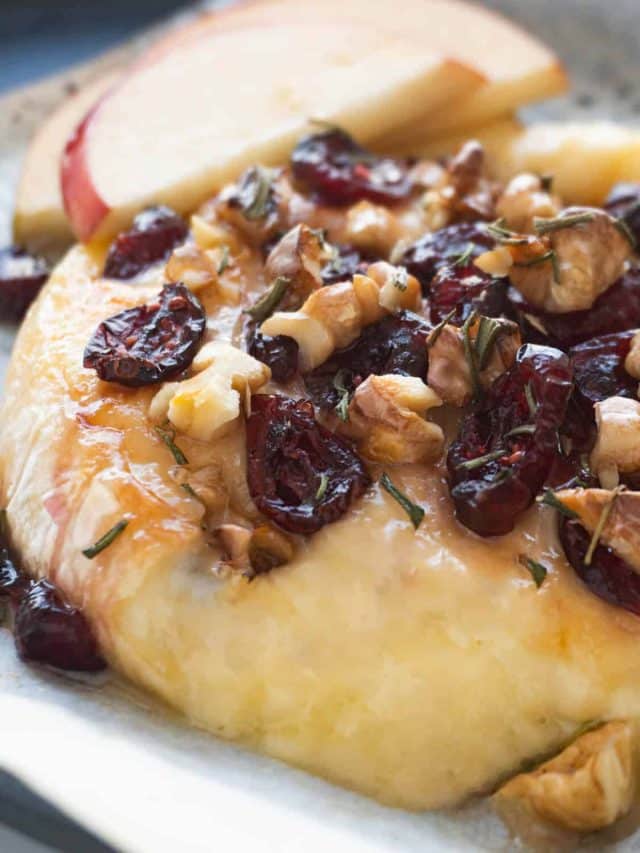 A closeup of baked brie topped with cranberries and walnuts.