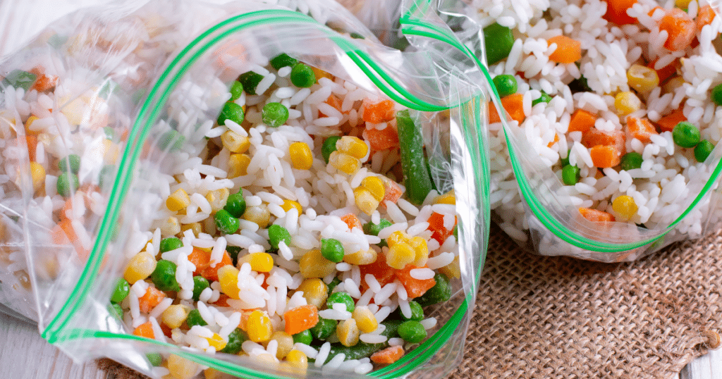 Freezer bags full of rice and vegetables on a tan surface.